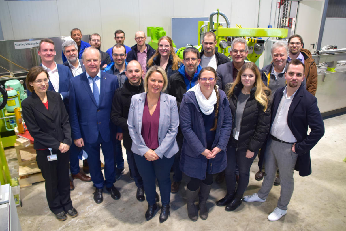 16 Personen aus den Projektteams stehen zusammen in einer Fertigungshalle der Technischen Universität Bergakademie Freiberg.